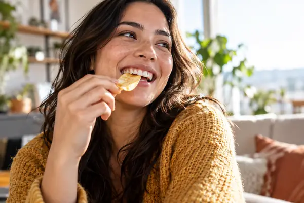 Candid close-up of a smiling person enjoying a crisp snack in bright natural light.
