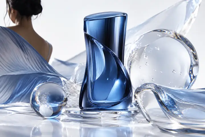 Sculptural blue beauty packaging surrounded by glossy transparent shapes on a clean white background.